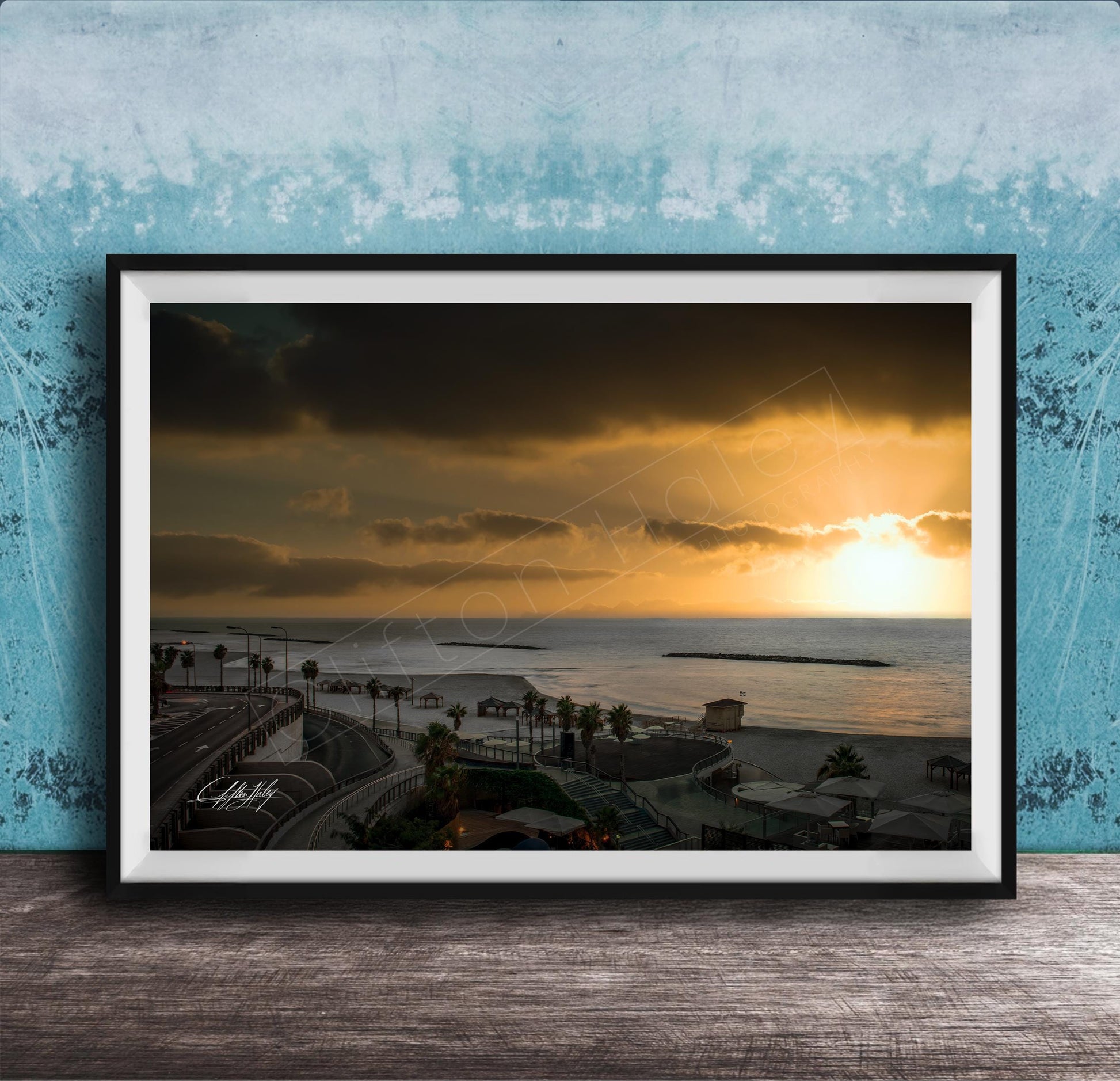 The image is a framed photograph of a beach at sunset, with palm trees and a body of water in the background.