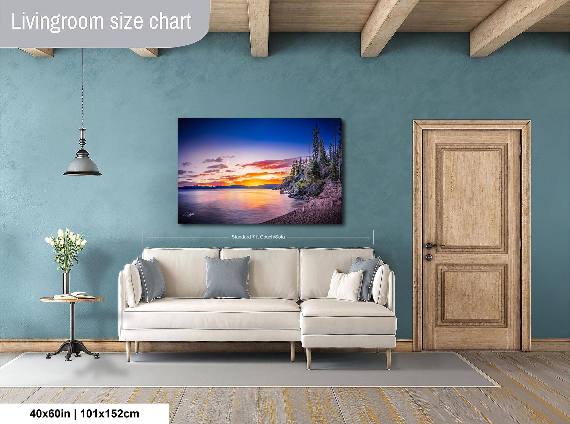 a living room with a large painting of a sunset landscape hanging on the wall. The painting is framed in a white frame and measures 40 inches by 101.5 centimeters. The room has a white sofa, a wooden door, and a small table with a vase of flowers.