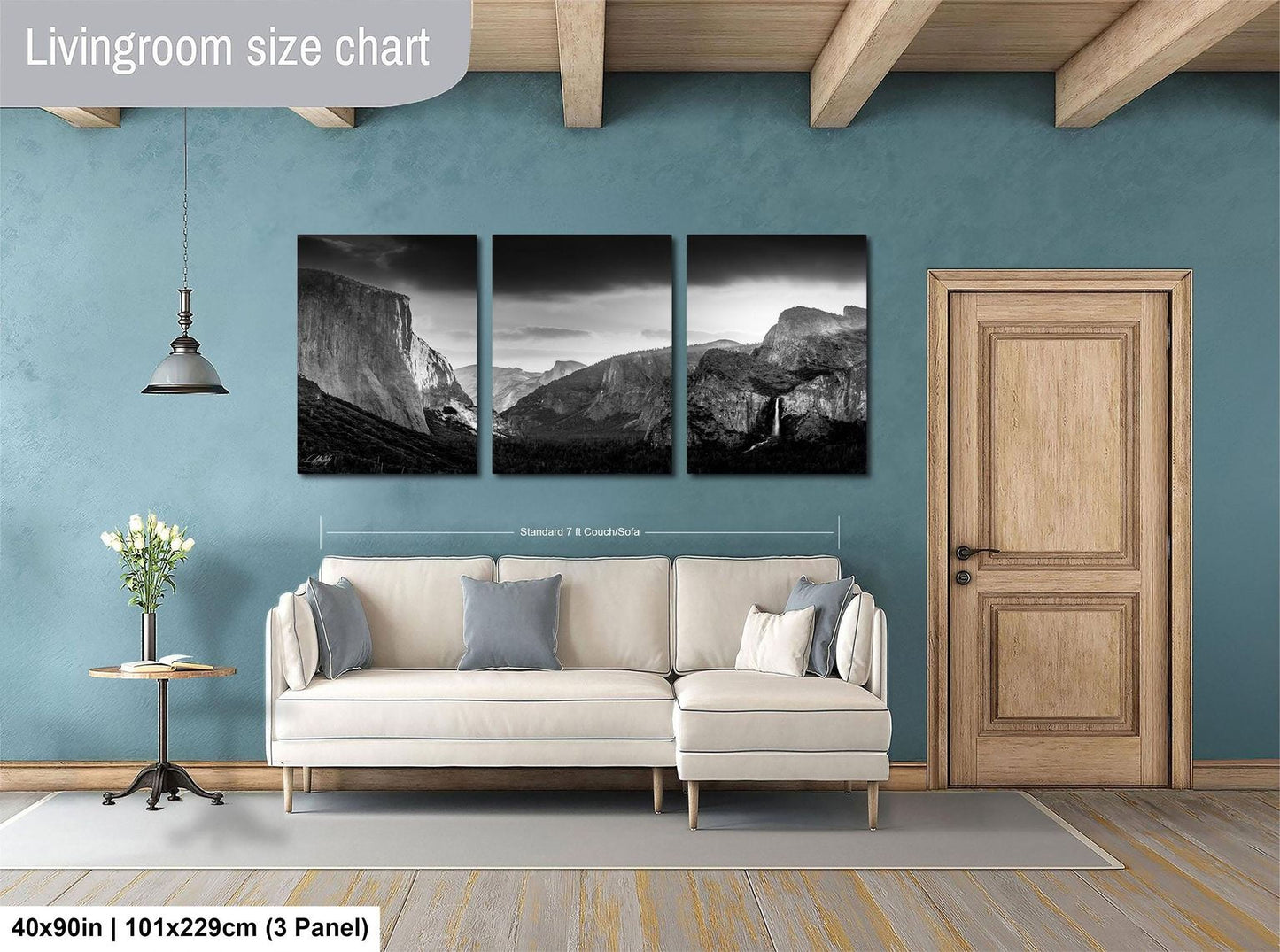 The image is a living room with a large, white sofa and a wooden door. Above the sofa, there is a wall-mounted painting depicting a mountainous landscape. The wall is painted in a light blue color, and the room has wooden beams on the ceiling.