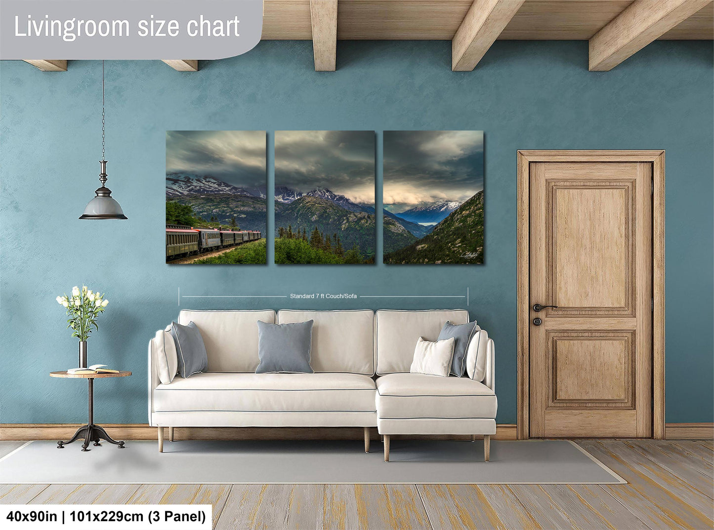 The image is a living room with a large white sofa, a wooden door, and a wall with a triptych of landscape paintings depicting mountains and a train.