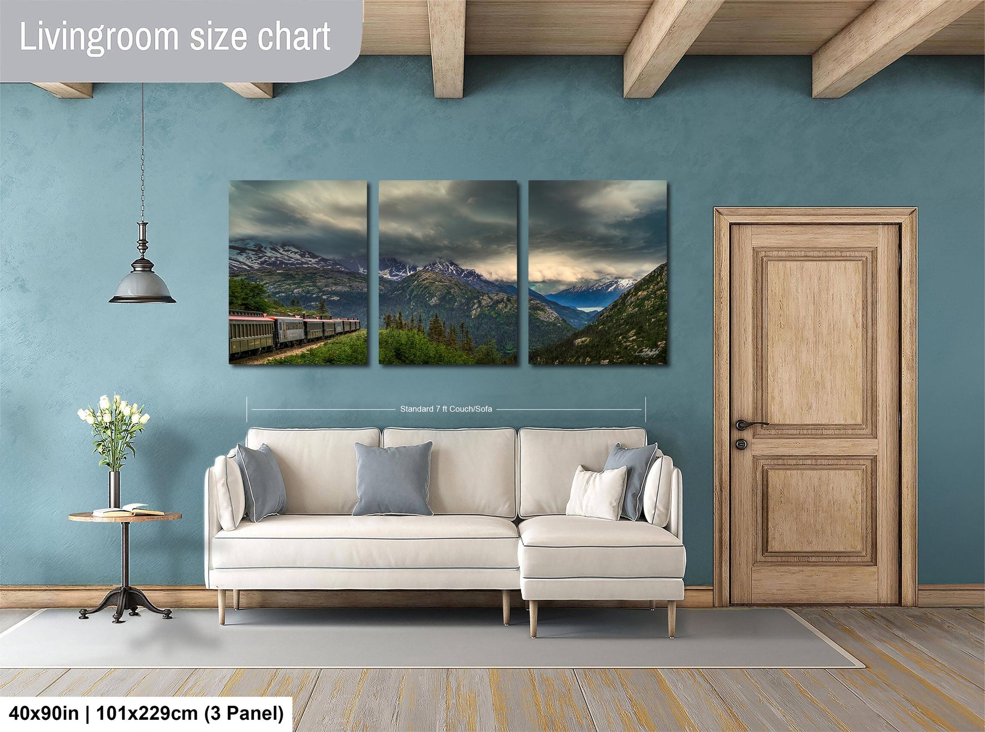 The image is a living room with a large white sofa, a wooden door, and a wall with a triptych of landscape paintings depicting mountains and a train.