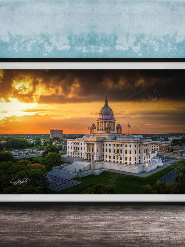 A framed photograph of a large, ornate building with a domed roof, set against a dramatic sky with orange and yellow hues, likely at sunset.