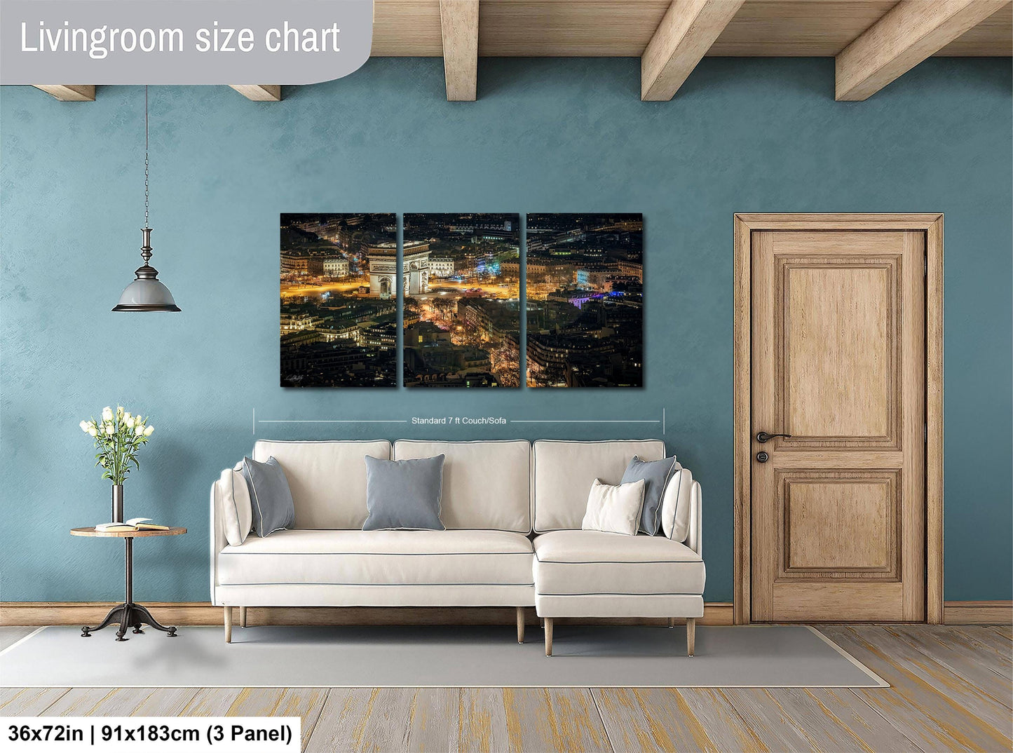The image is a living room with a large white sofa, a wooden door, and a large wall art depicting a cityscape at night.