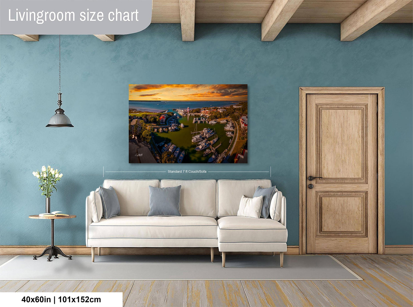 a living room with a large wall painting depicting a scenic landscape, a white sofa, a wooden door, and a small table with a vase of flowers.