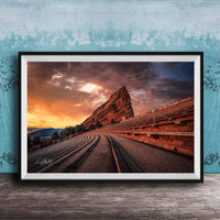 a large, steep rock formation with a winding path leading up to it, set against a dramatic sky with orange and blue hues.