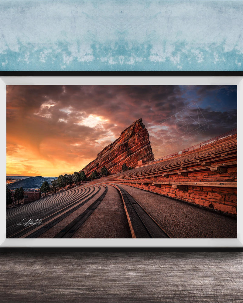 a large, steep rock formation with a winding path leading up to it, set against a dramatic sky with orange and blue hues.