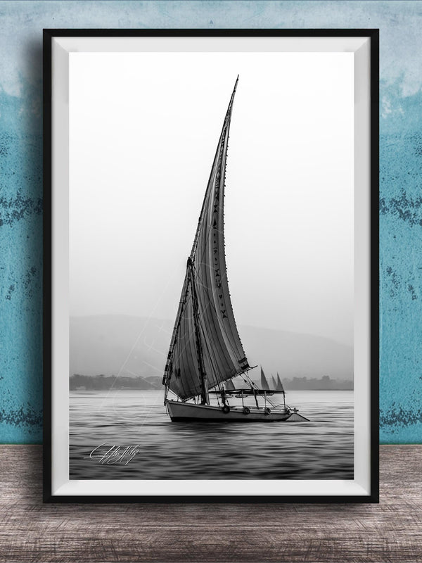 This luxury black and white fine art photograph captures a felucca sail boat drifting along the Nile River at sunset near Luxor, Egypt. Soft fog and minimalist composition create a timeless, monochrome aesthetic rooted in Egyptian river culture. Ideal for collectors and interior designers seeking refined, museum-quality wall art that embodies elegance, simplicity, and enduring calm.