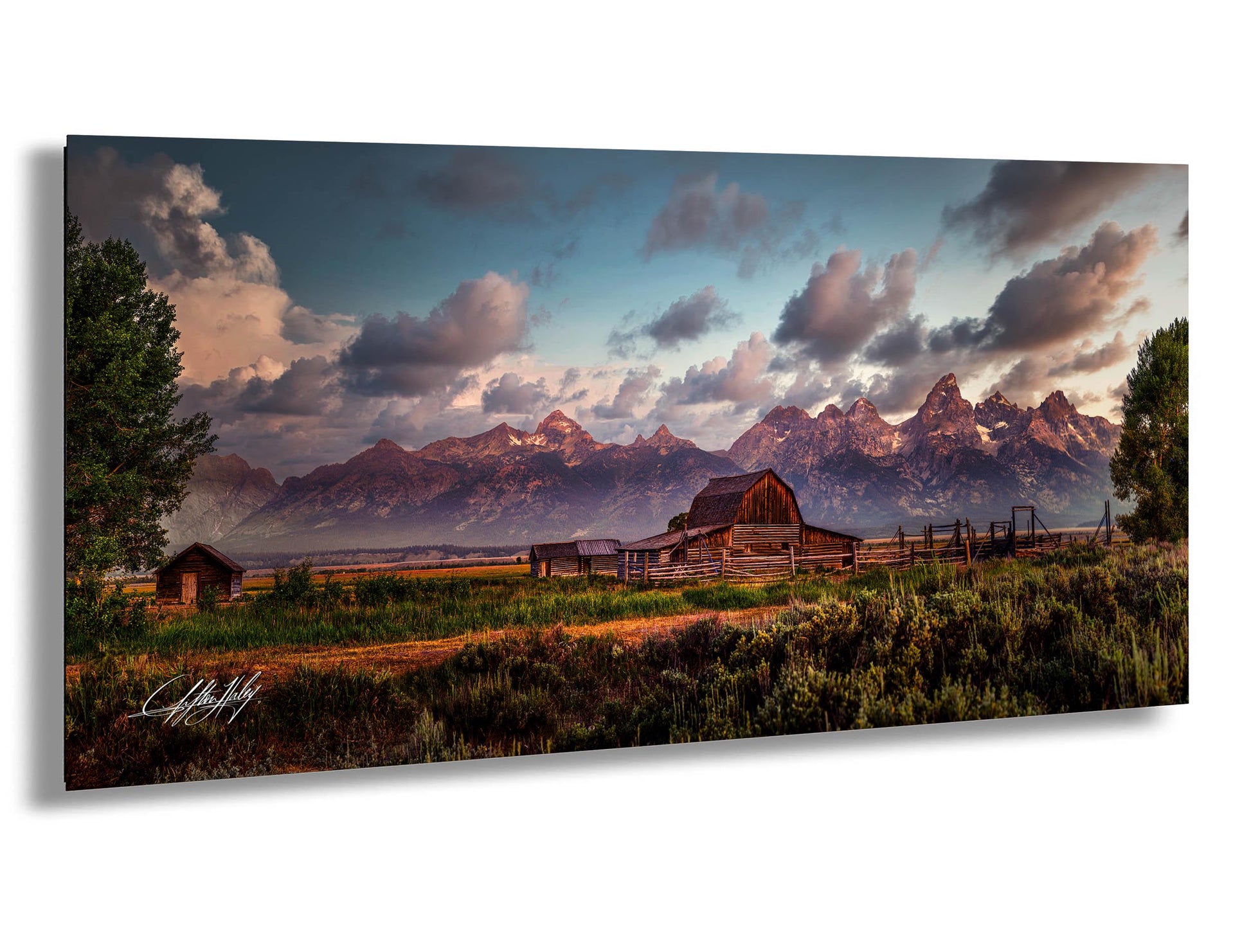 A picturesque rural landscape with a wooden barn, a small shed, and a dirt road leading to a mountain range in the distance. The sky is filled with clouds, and the sun is setting, casting a warm glow over the scene.