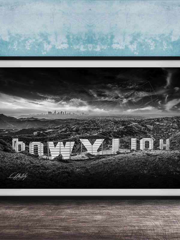 A black and white photograph of the Hollywood Sign, a famous landmark in Los Angeles, California. The sign is prominently displayed in the foreground, with the city skyline visible in the background.