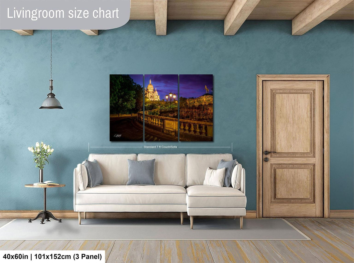The image is a living room with a white sofa, a wooden door, and a large wall art depicting a cityscape at night.