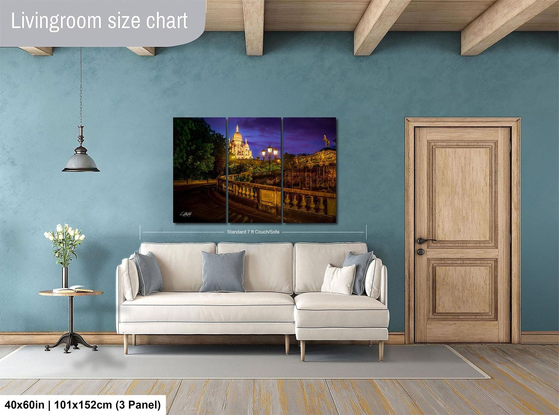 The image is a living room with a white sofa, a wooden door, and a large wall art depicting a cityscape at night.