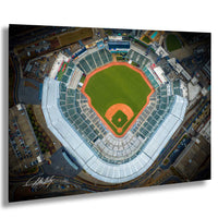 An aerial view of a baseball stadium with a green field, red dirt around the home plate, and surrounding buildings and parking lots.