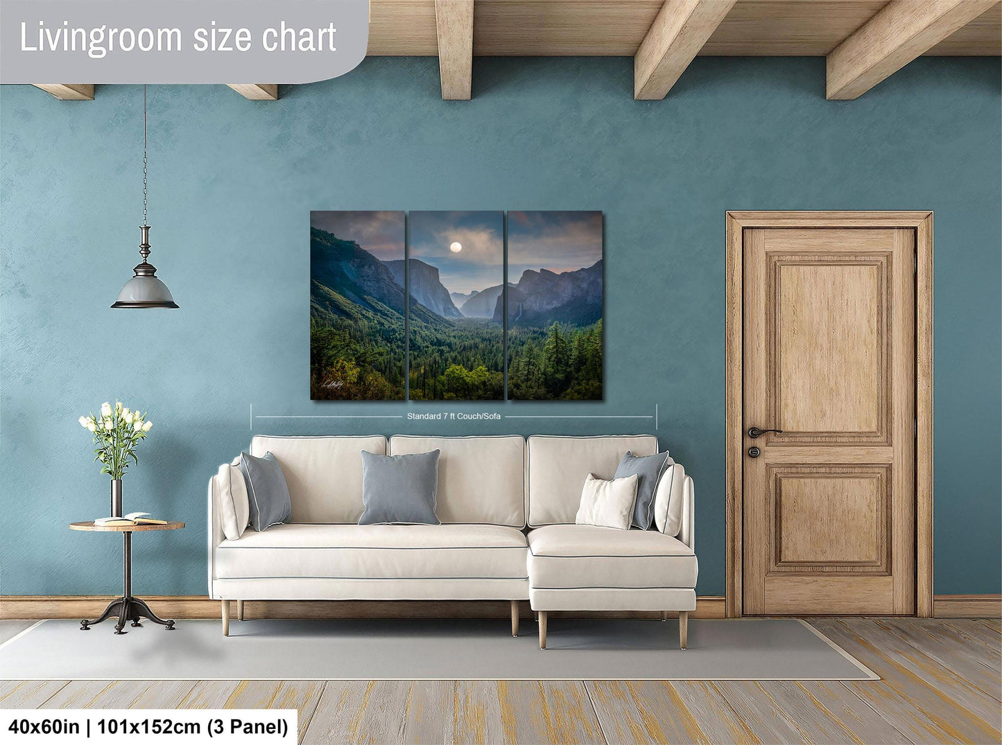 The image is a living room with a large painting of a mountain landscape hanging on the wall. The painting is divided into three panels, and the living room has a white sofa, a wooden door, and a small table with a vase of flowers.
