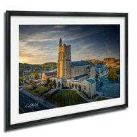 a large, multi-story stone church with a tall tower, set against a backdrop of a city skyline and a sunset sky.