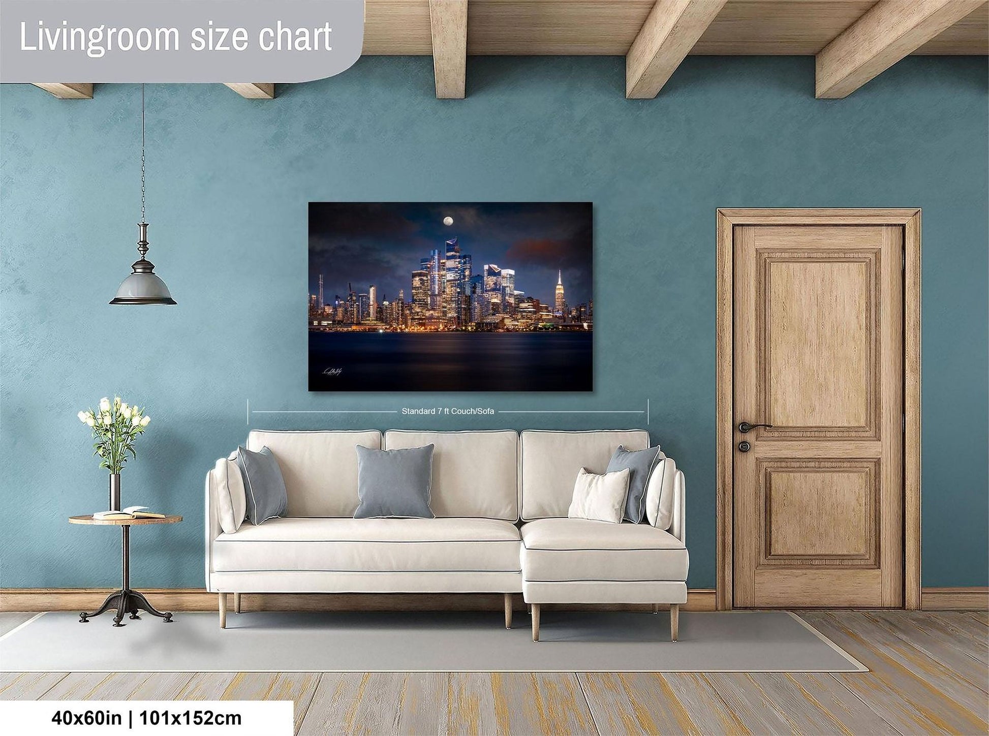 a living room with a large city skyline painting hanging on the wall. The painting is framed and measures 40 inches by 101.5 centimeters. The room has a white sofa, a wooden door, and a small table with a vase of flowers.