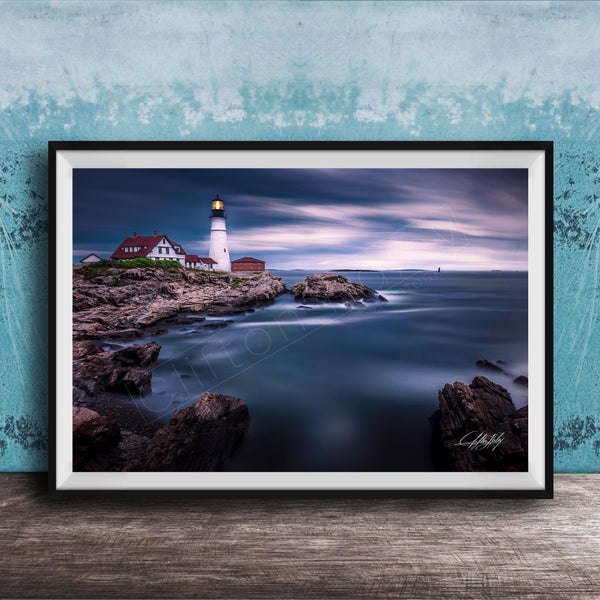 A framed photograph depicting a lighthouse on a rocky coastline, with the ocean and a cloudy sky in the background.