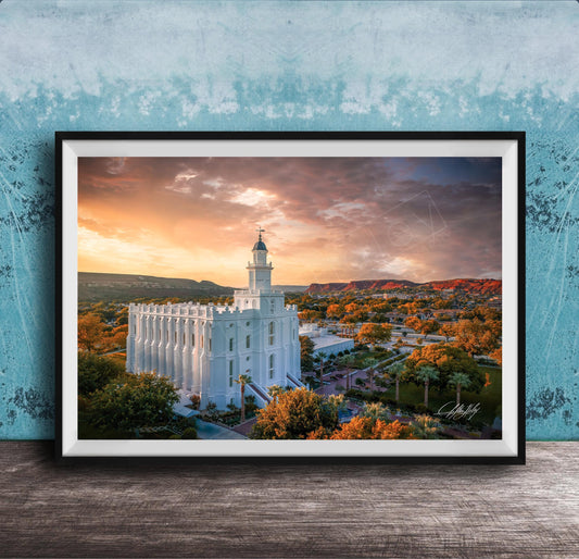 A framed photograph of a white temple with a tower, set against a colorful sunset sky with clouds and mountains in the background.