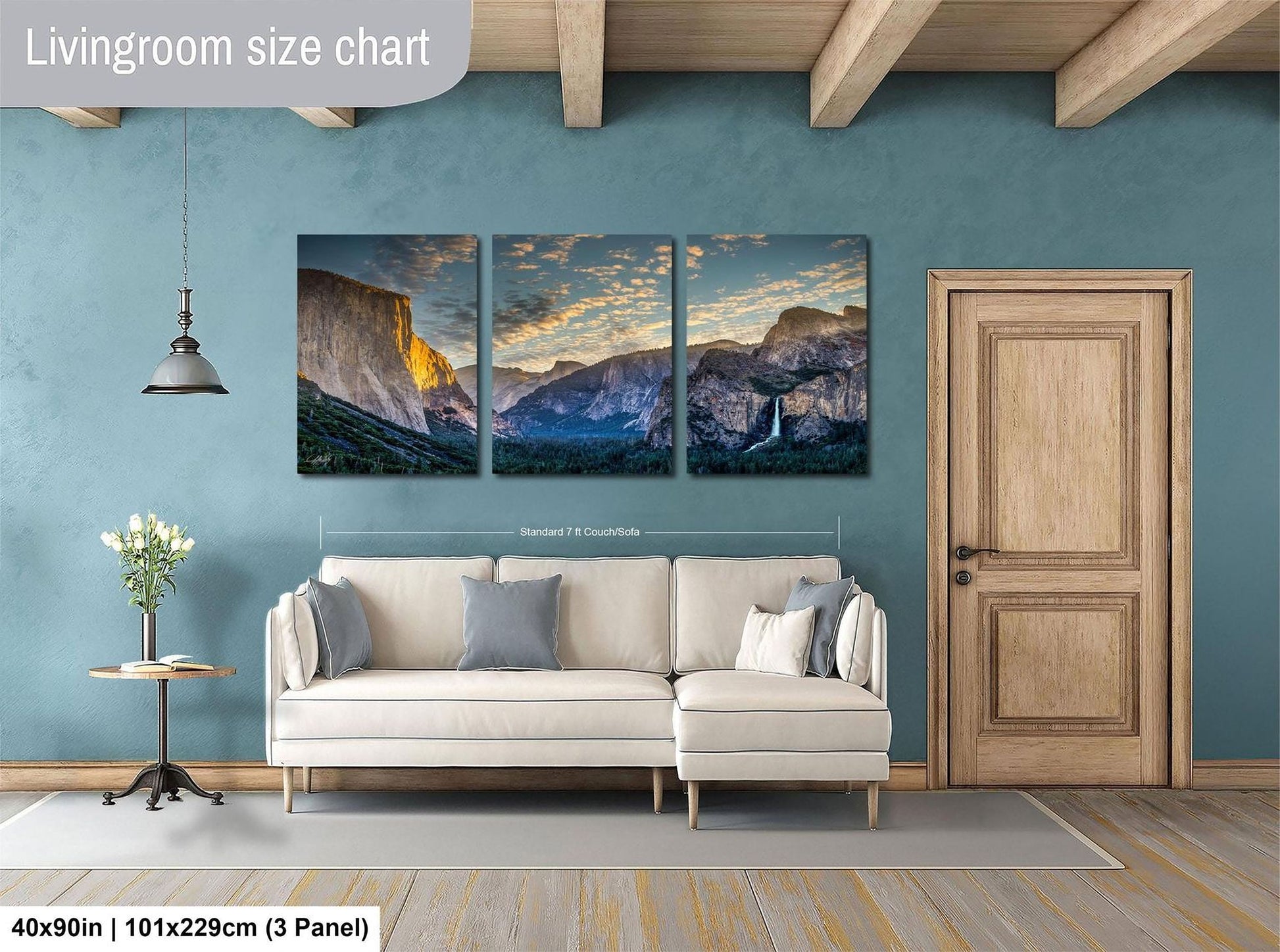 The image is a living room with a large wall art depicting a scenic mountain landscape. The wall art is divided into three panels, each showcasing a different part of the mountain range. The living room has a white sofa and a wooden door, creating a cozy and inviting atmosphere.