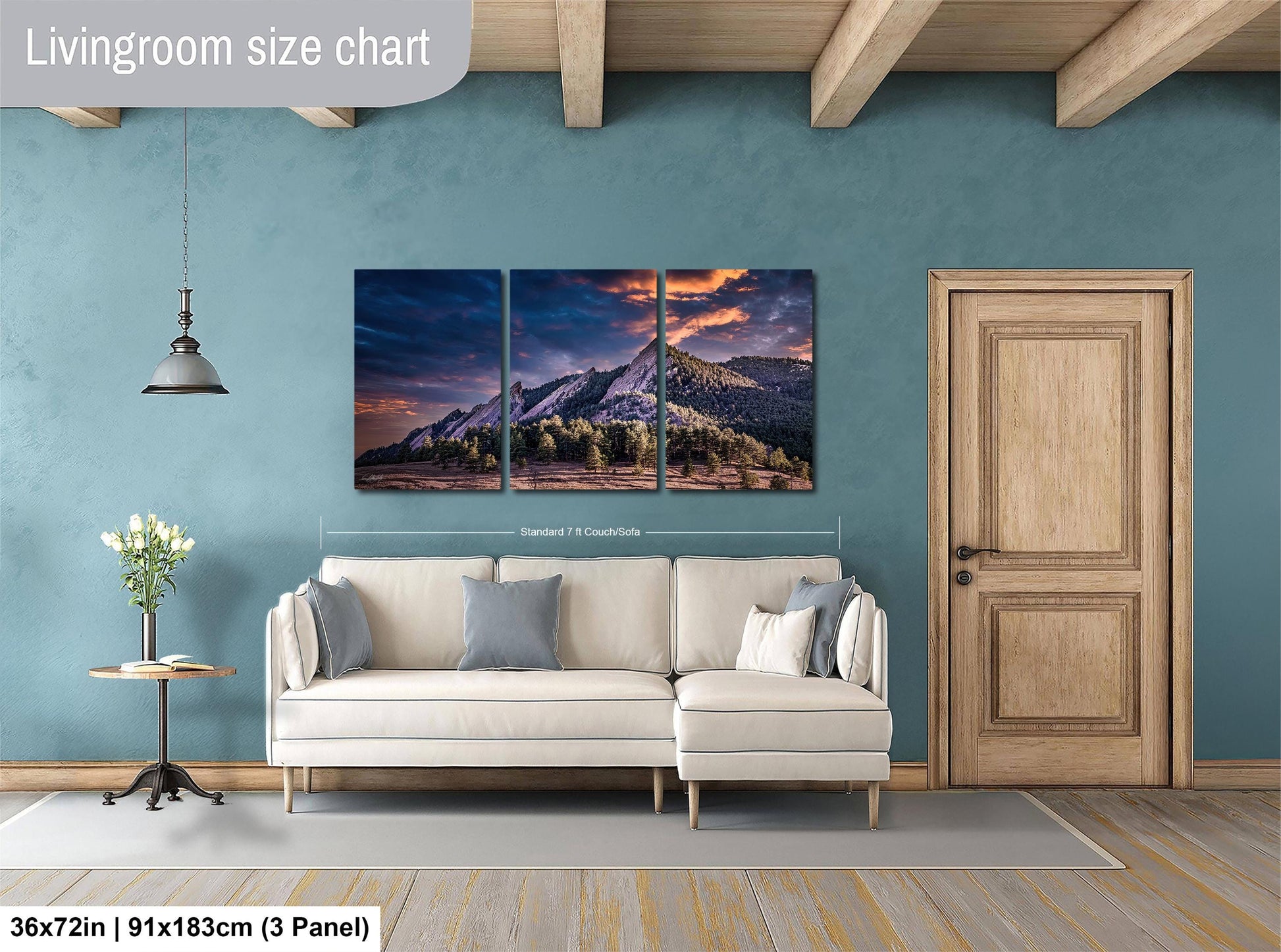 The image is a living room with a large, three-panel landscape painting hanging on the wall. The painting depicts a mountainous scene with a sunset. The room has a white sofa and a wooden door, and there is a vase of flowers on a table. The painting is approximately 36 inches wide and 91 inches tall, and it is mounted on a wooden panel.