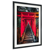 A framed photograph depicting a red torii gate leading down a set of stairs, surrounded by trees and foliage.