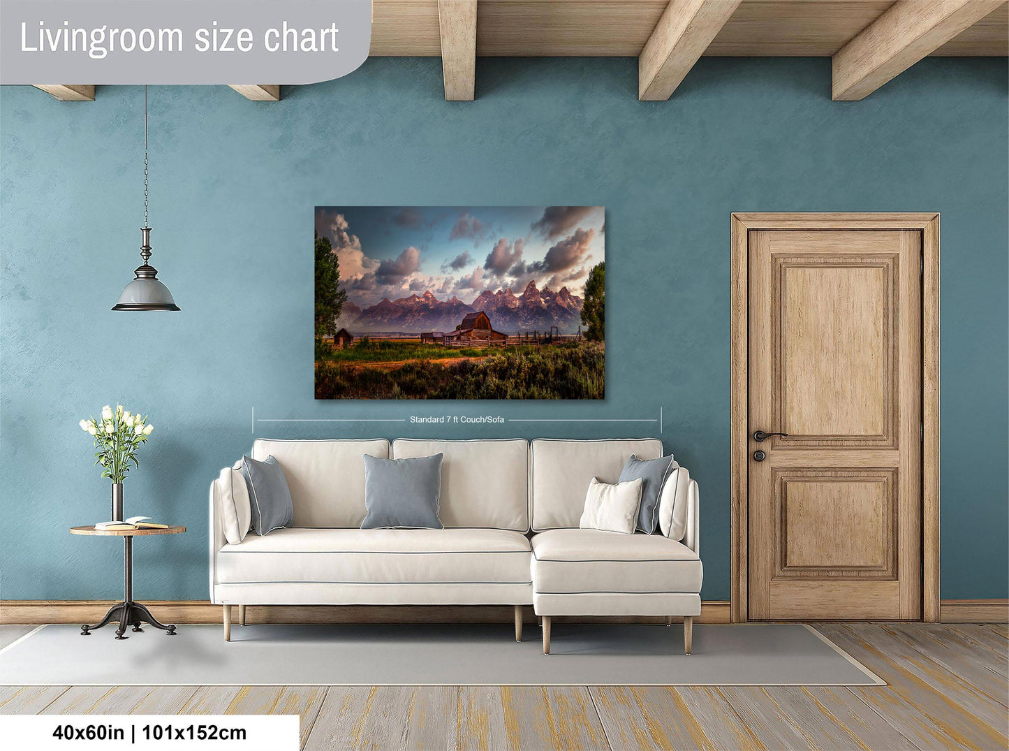 a living room with a large landscape painting hanging on the wall. The painting features a mountain range and a building in the distance. The room has a white sofa and a wooden door, creating a cozy and inviting atmosphere.