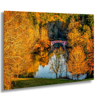 A picturesque autumn landscape with a tranquil lake surrounded by vibrant orange and yellow trees. A red brick bridge spans the lake, creating a serene and peaceful atmosphere.