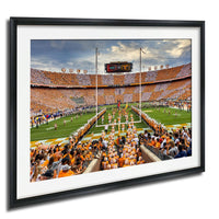 A framed photograph of a football game in progress, with a large crowd of spectators filling the stands and players on the field.