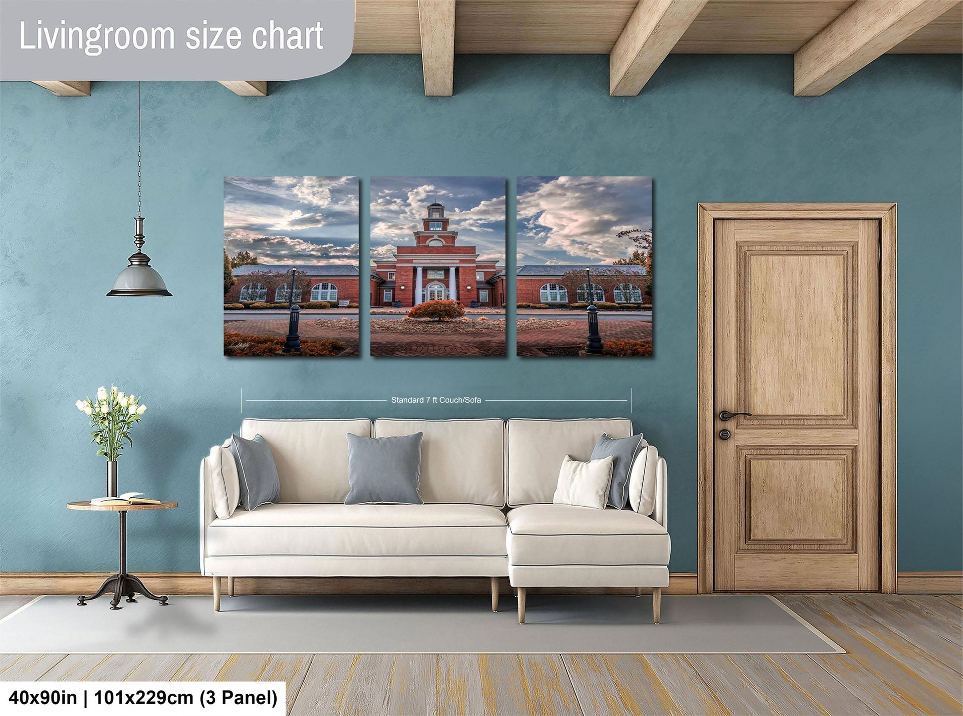 The image is a living room with a white sofa and a wooden door. Above the sofa, there is a triptych of paintings depicting a building and a sky with clouds. The wall behind the sofa has a blue color, and there is a lamp hanging from the ceiling. The image is described as a living room size chart, which means it provides a visual representation of the dimensions of the living room.