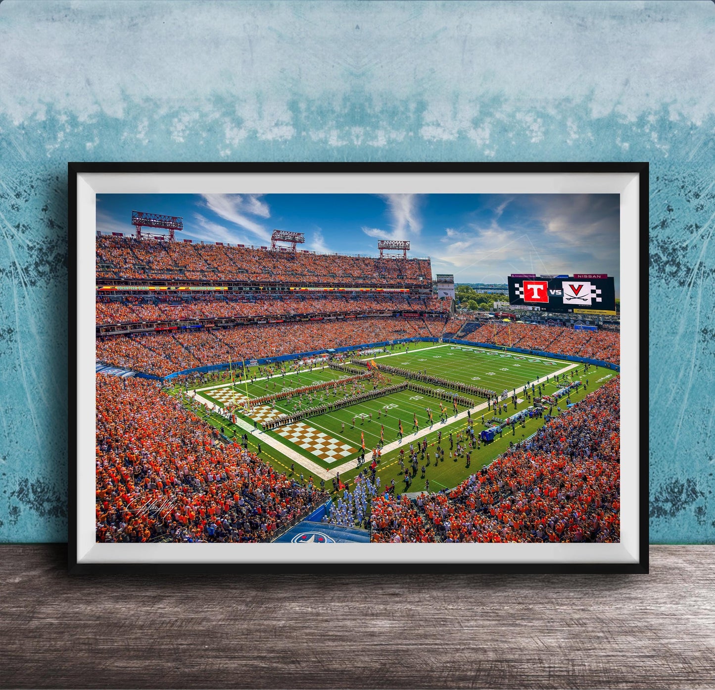 A framed photograph of a crowded football stadium during a game, with the field and stands filled with spectators.