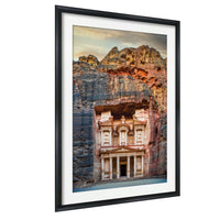 a large, ancient stone structure carved into a cliff face, with a carved doorway and columns. The structure appears to be a temple or monument, and the photograph is framed and displayed on a wall.
