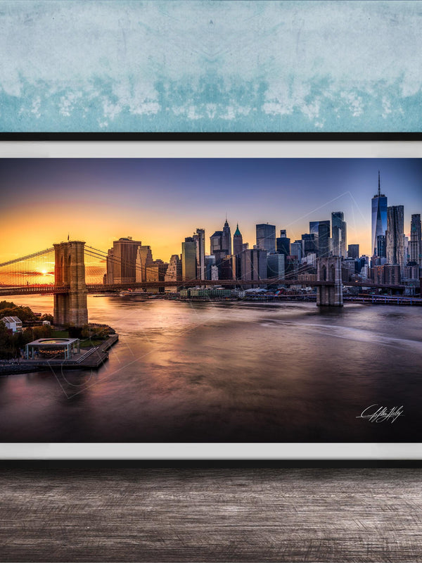 A framed photograph of the skyline of New York City at sunset, with the Brooklyn Bridge and other skyscrapers visible in the background.