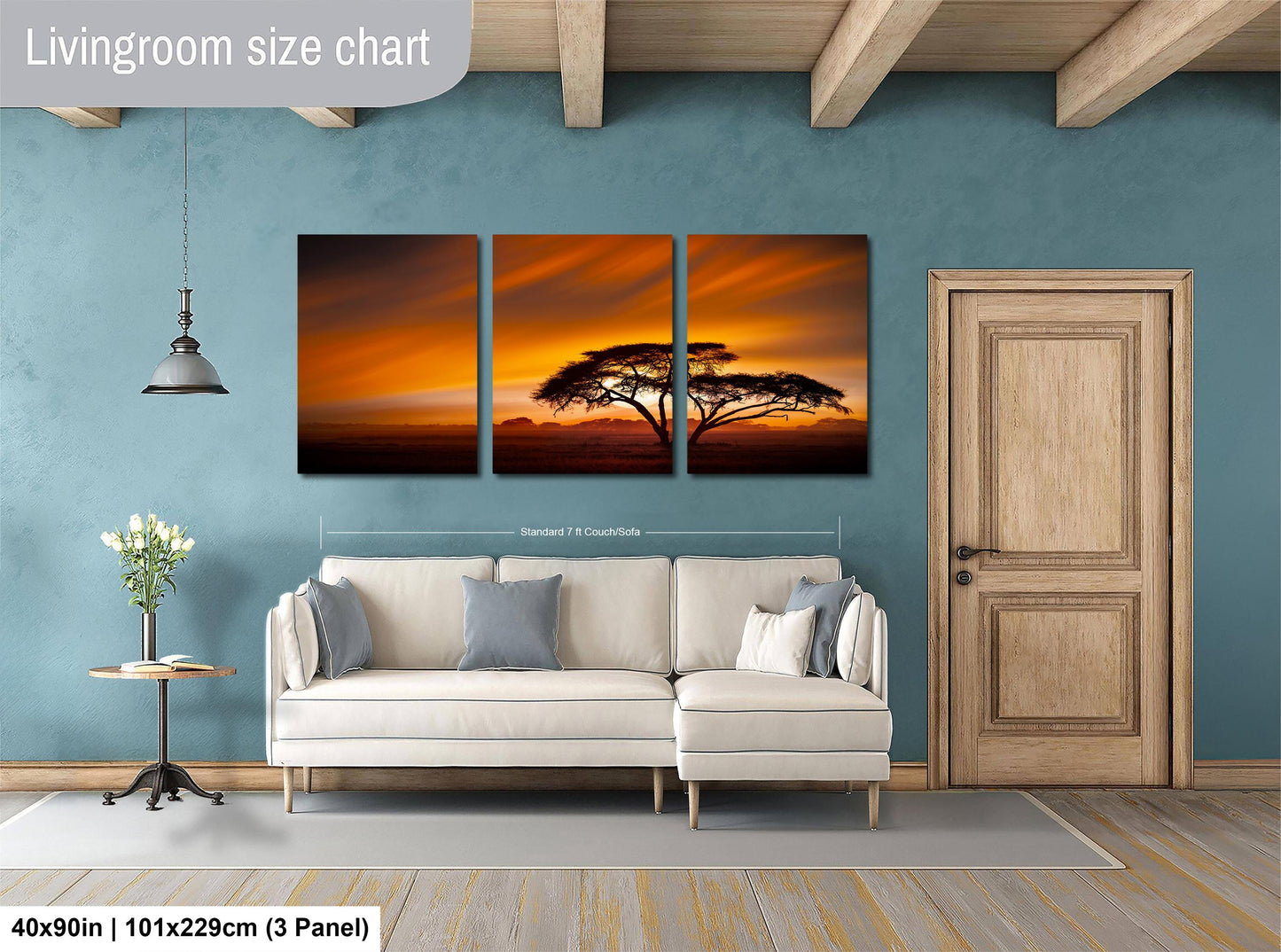 The image is a living room with a large white sofa and a wooden door. Above the sofa, there is a triptych of paintings depicting a sunset over a landscape. The wall behind the sofa has a blue color, and there is a potted plant and a vase on the floor. The image is labeled as a livingroom size chart, indicating that it is a scale model or a representation of the actual room size.