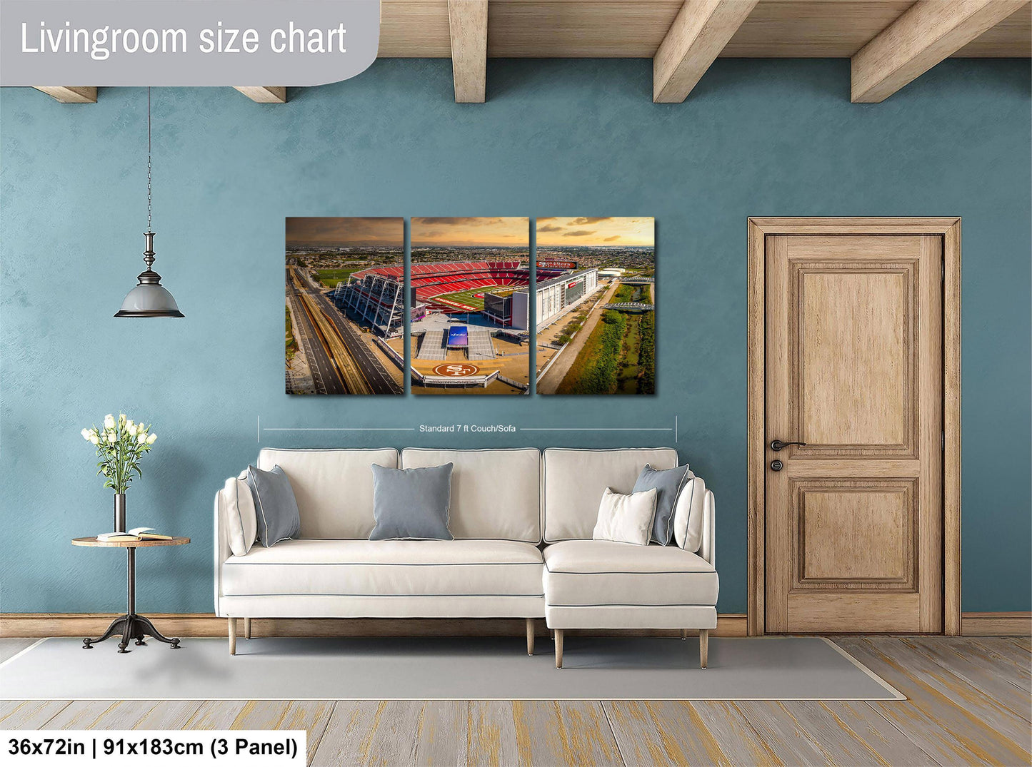 The image is a living room with a large white sofa, a wooden door, and a wall-mounted three-piece wall art depicting a stadium.