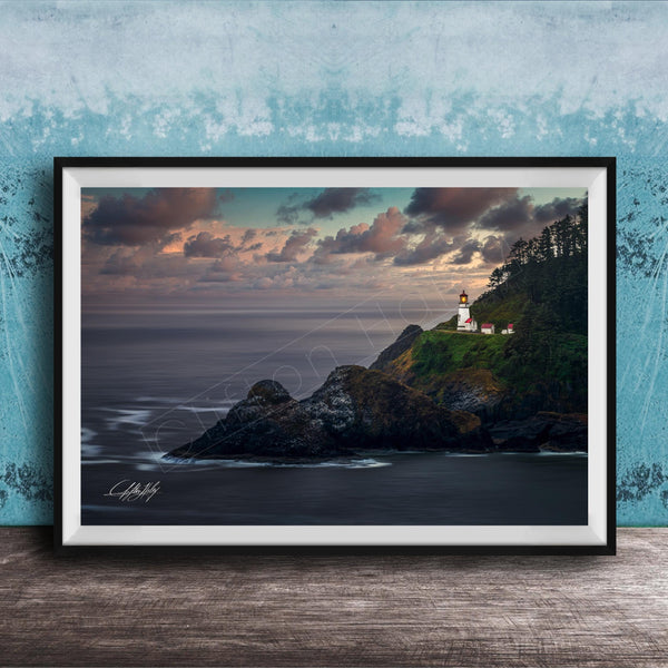 A framed photograph depicting a lighthouse on a cliff overlooking the ocean at sunset.