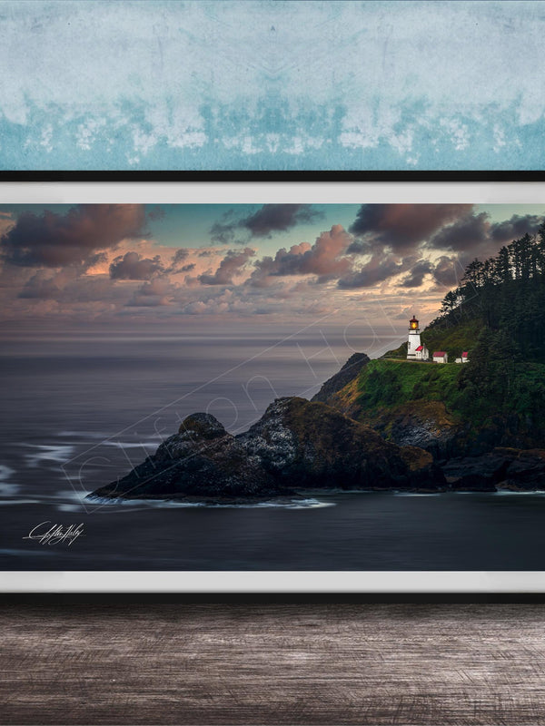 A framed photograph depicting a lighthouse on a cliff overlooking the ocean at sunset.