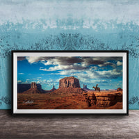 A framed photograph of a desert landscape with a cowboy on a horse, set against a blue and white patterned background.