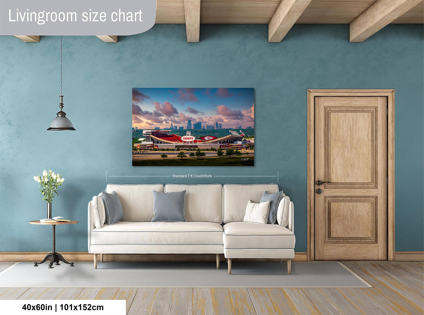 a living room with a large wall-mounted painting depicting a stadium or sports venue. The painting is framed and hangs above a white sofa, which is positioned in front of a wooden door. The room has a wooden floor and a small table with a vase of flowers. The wall has a blue color, and the overall layout and design of the room suggest a modern and stylish interior.
