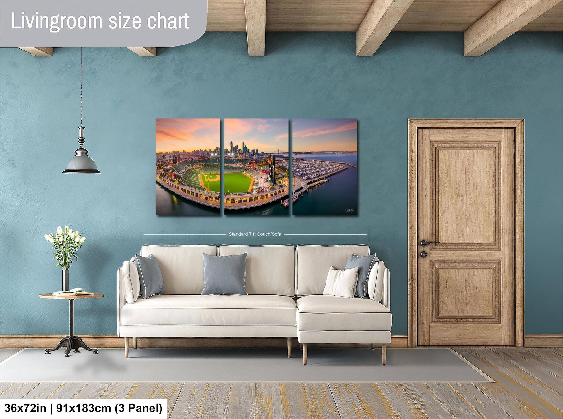 The image is a living room with a large wall art depicting a city skyline at sunset. The wall art is a collage of three panels, with the largest panel spanning approximately 36 square inches. The smaller panels are also visible, but their exact size cannot be determined from the image.