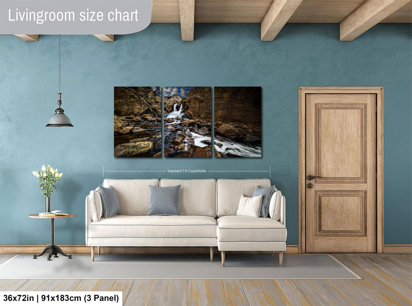 The image is a living room with a large white sofa, a wooden door, and a painting of a waterfall on the wall.