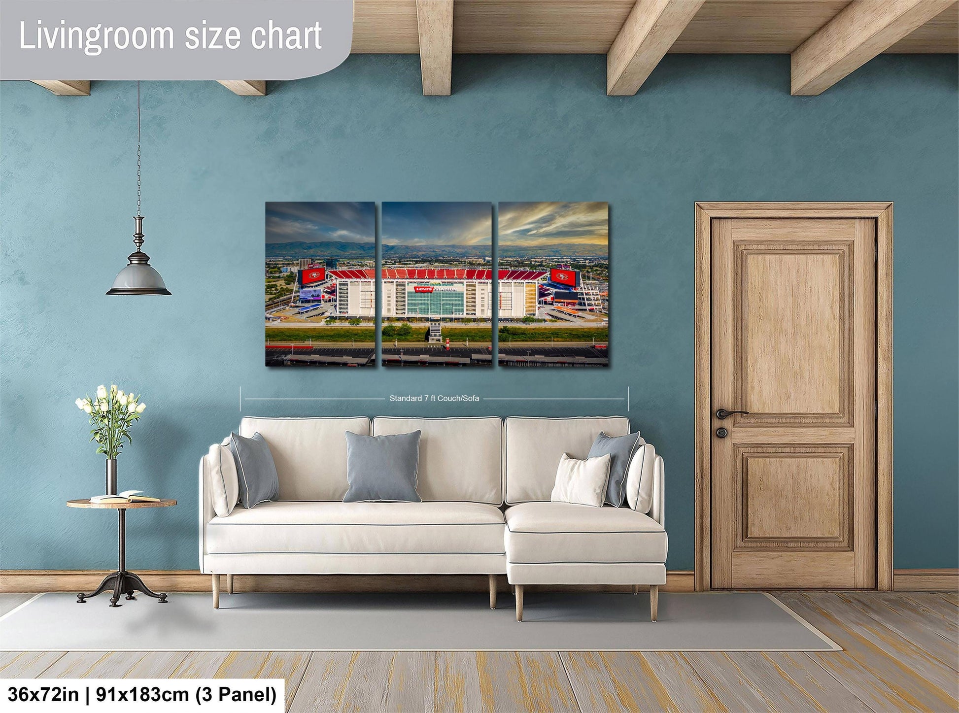The image is a living room with a large wall art depicting a stadium. The wall art is a collage of three panels, each showing different aspects of the stadium. The living room has a white sofa and a wooden door, and there is a potted plant and a vase on a table. The wall art is approximately 36 inches wide and 9 inches tall, and it is mounted on a blue wall.