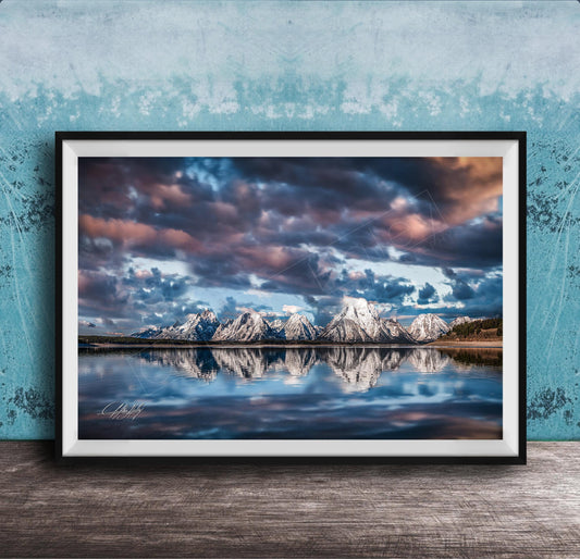 A framed photograph of a serene landscape with snow-capped mountains reflected in a calm lake, set against a dramatic sky with clouds.