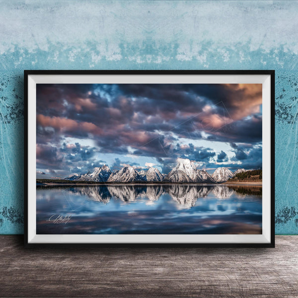 A framed photograph of a serene landscape with snow-capped mountains reflected in a calm lake, set against a dramatic sky with clouds.