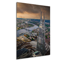 The image is an aerial view of a city skyline, featuring a tall, modern skyscraper with a distinctive glass and steel structure. The cityscape is surrounded by a body of water, and the sky is filled with clouds, creating a dramatic and atmospheric scene.