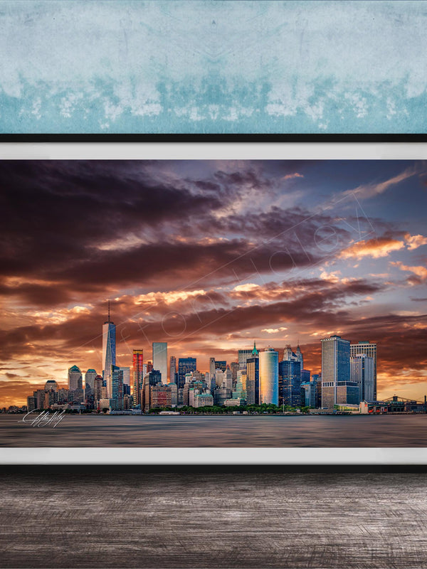 A framed photograph of the New York City skyline at sunset, with the city's skyscrapers silhouetted against a dramatic sky filled with clouds and vibrant colors.