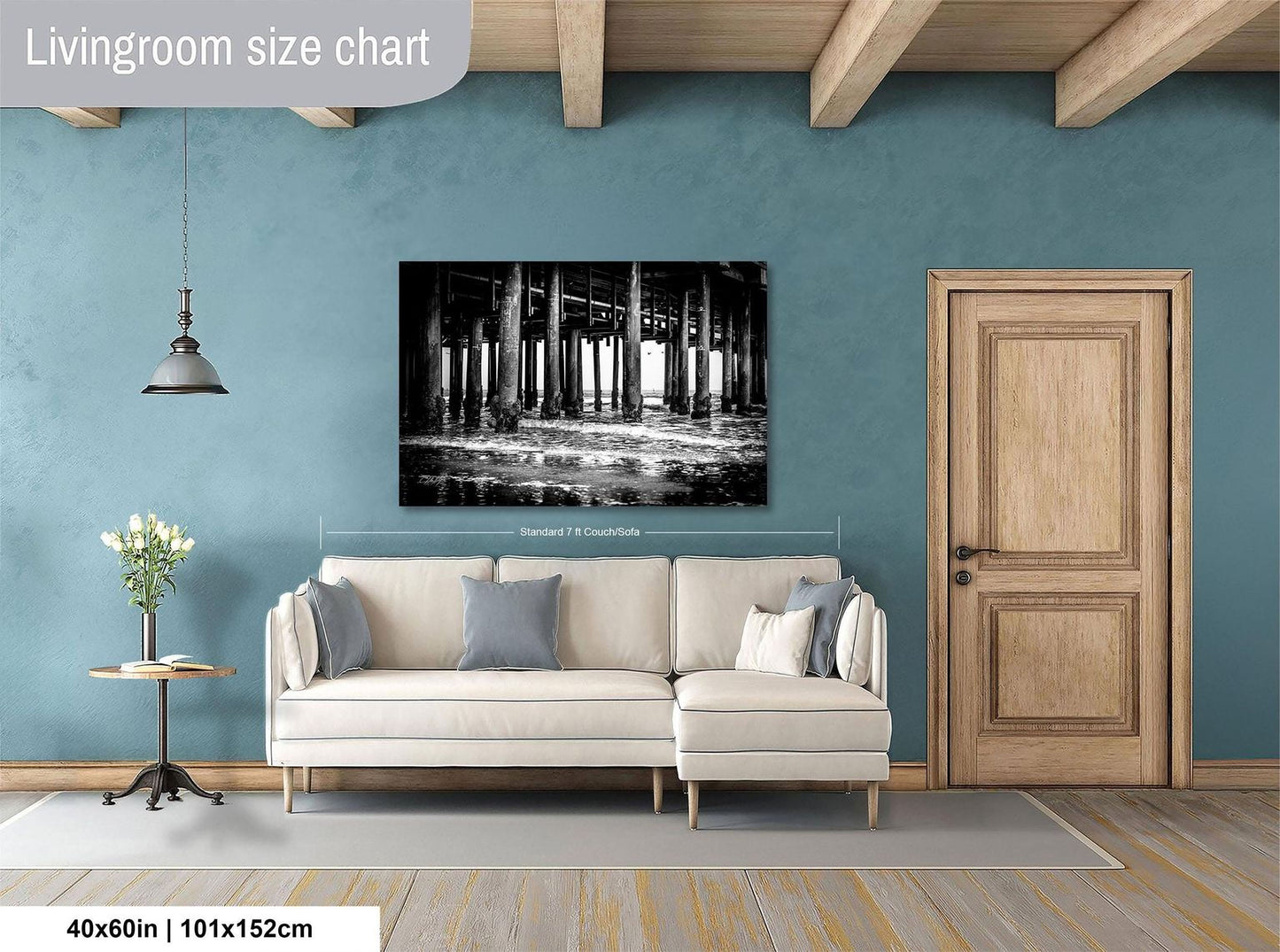 a living room with a large black and white photograph of a pier or bridge hanging on the wall. The photograph is framed and measures 40 inches by 101.5 centimeters. The living room is furnished with a white sofa and a wooden door, creating a cozy and inviting atmosphere.