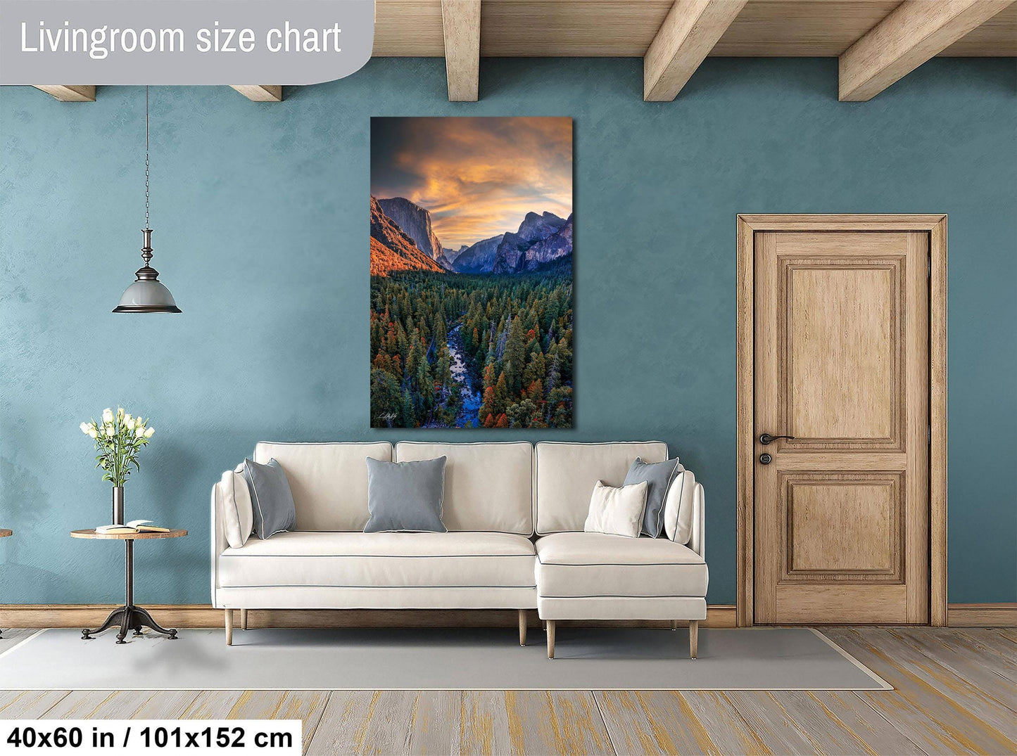 a living room with a large wall painting of a mountainous landscape, a white sofa, a wooden door, and a small table with a vase of flowers.