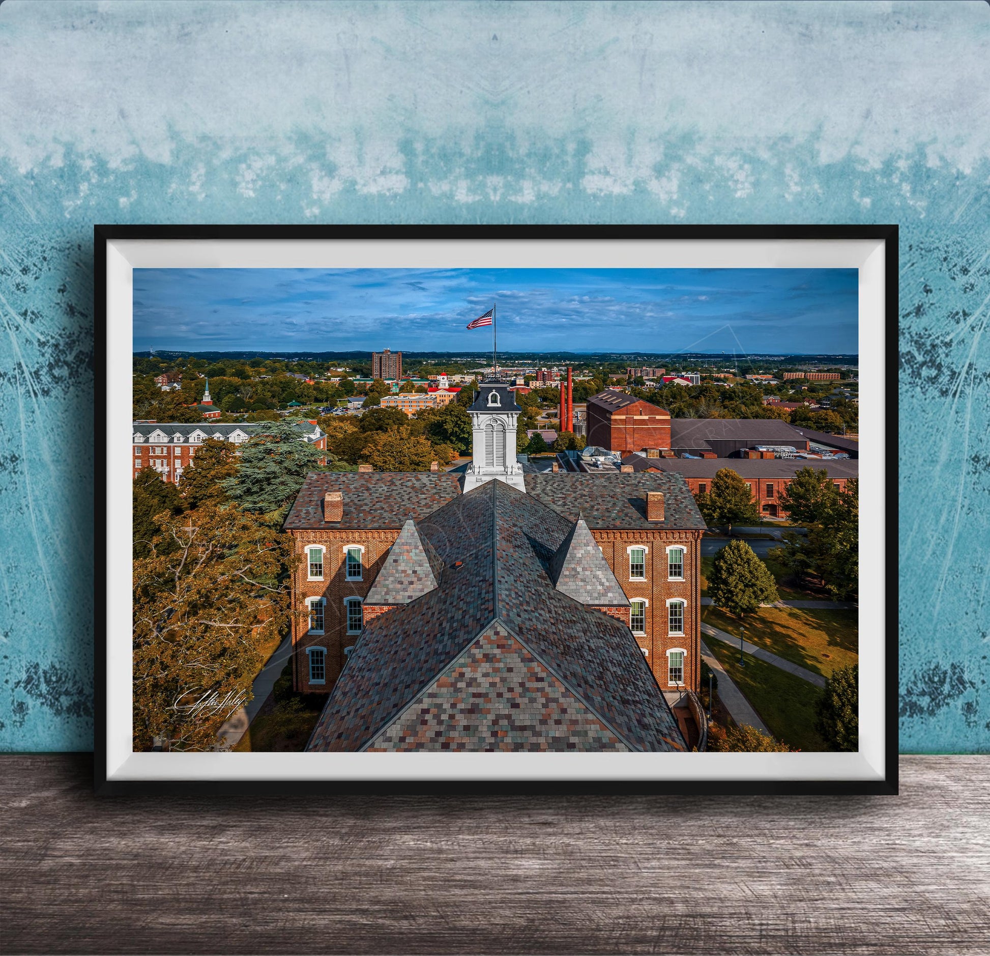 The image is a framed aerial view of a city, showcasing a mix of buildings, trees, and a prominent clock tower.