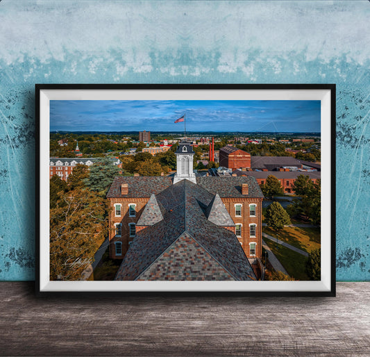 The image is a framed aerial view of a city, showcasing a mix of buildings, trees, and a prominent clock tower.