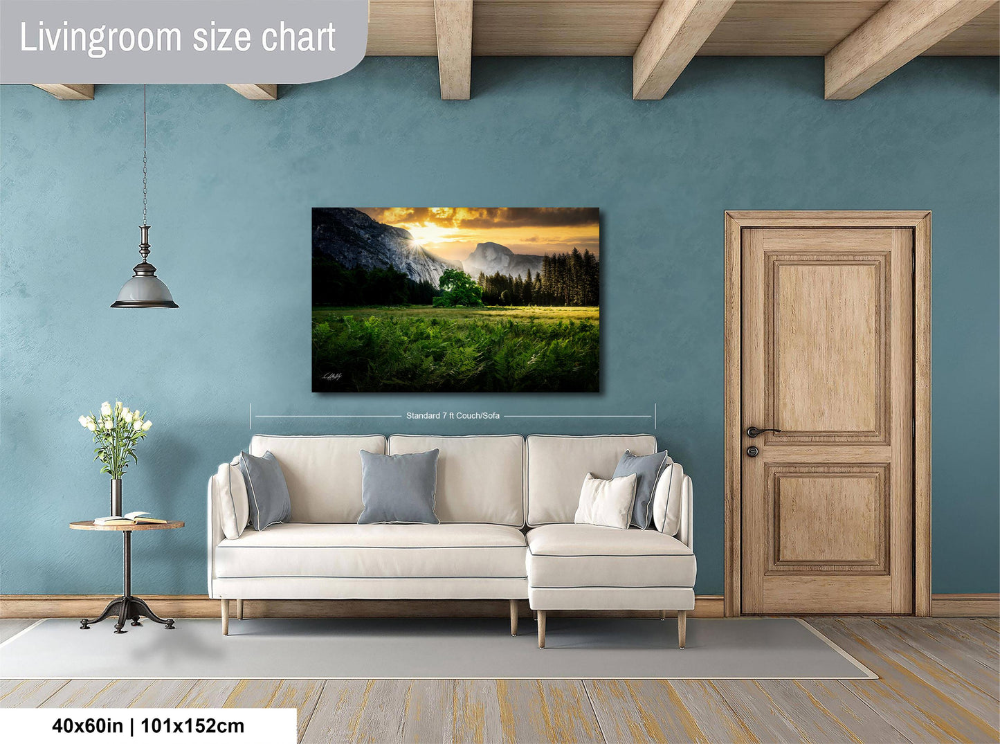 a living room with a large landscape painting hanging on the wall, a white sofa, a wooden door, and a small table with a vase of flowers.