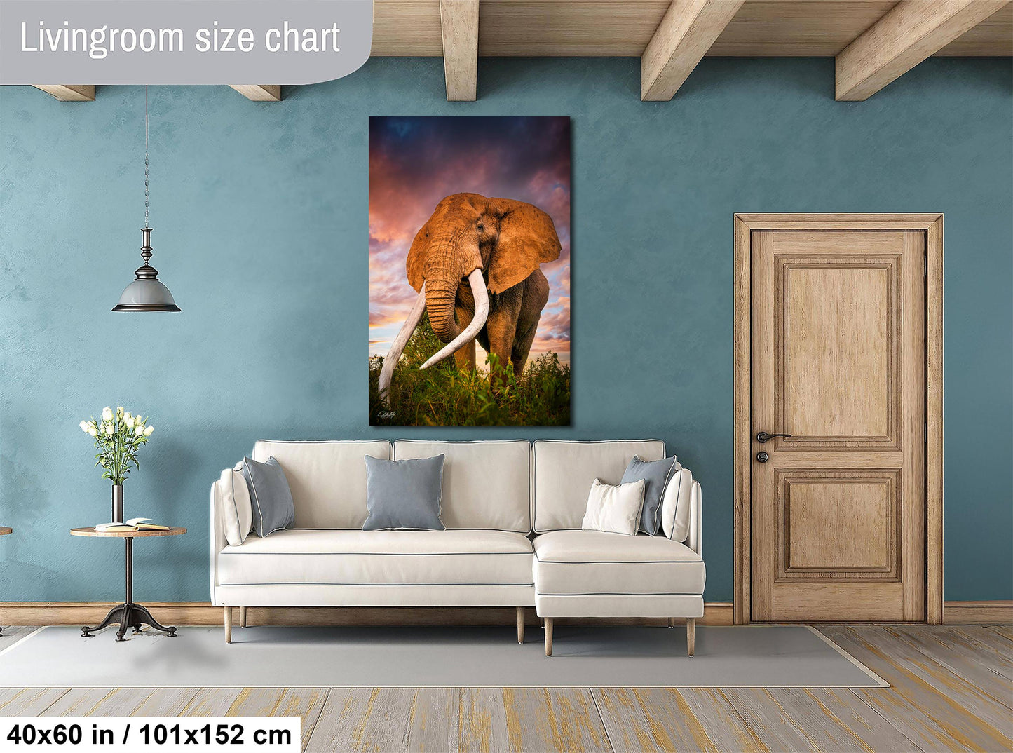 a living room with a large elephant painting hanging on the wall. The elephant is standing in a grassy field with trees in the background, creating a serene and natural atmosphere. The living room is furnished with a white sofa and a wooden door, providing a cozy and inviting space.